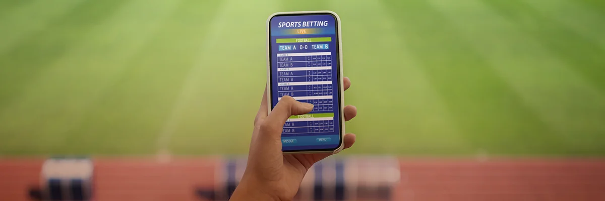 Person using a smartphone with a sports betting app displayed in a stadium