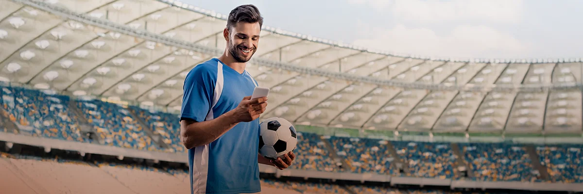 Man in a stadium checking his phone while holding a soccer ball