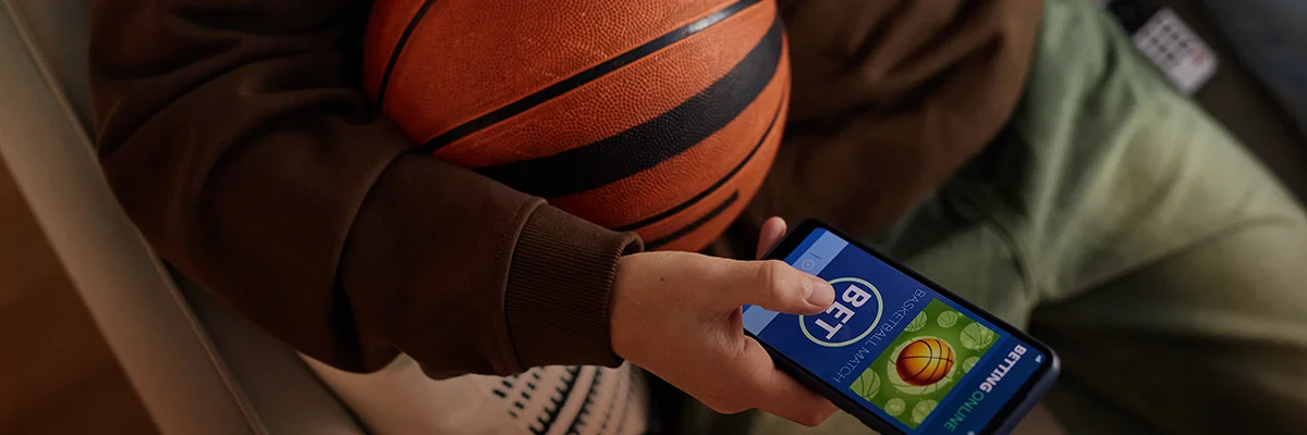 Person holding a basketball while checking a sports betting app on a smartphone