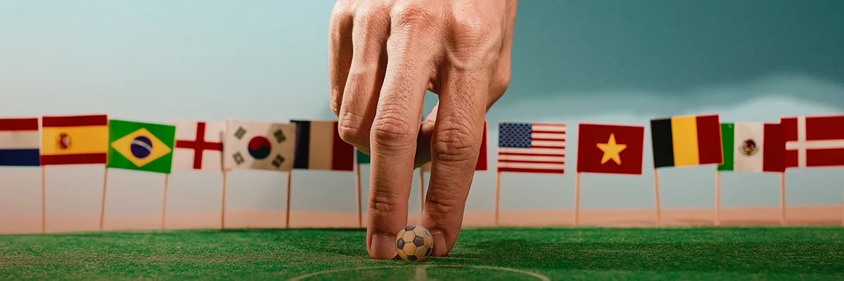 Hand placing a small soccer ball on a field with international flags in the background