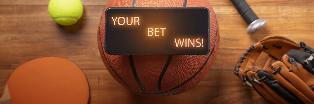 Smartphone showing a winning bet message on top of a basketball with various sports equipment